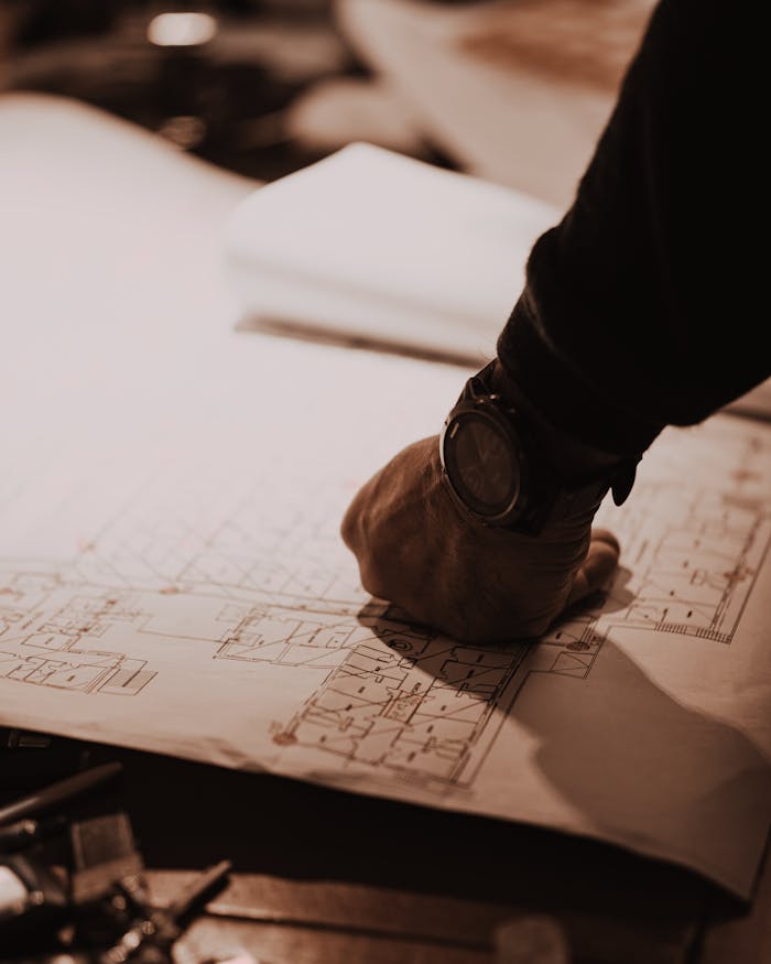 Close-up of architect's hand reviewing blueprints in a dimly lit workspace, focusing on detailed floorplans.